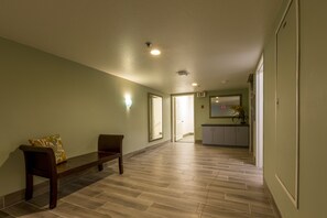 A hallway with a bench, a door, and a kitchen area in the background.