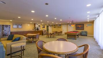A hotel lobby with a pool table, a bar area, and a seating area with tables and chairs.