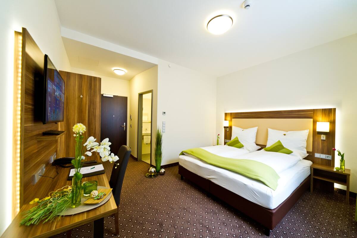 Een hotelkamer met een bed, nachtkastje, lamp en bureau met stoel.