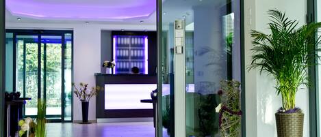 A modern reception area with a glass door, a reception desk, and a potted plant.