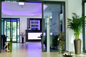 Un área de recepción moderna con puerta de vidrio, mostrador de recepción y planta en maceta.