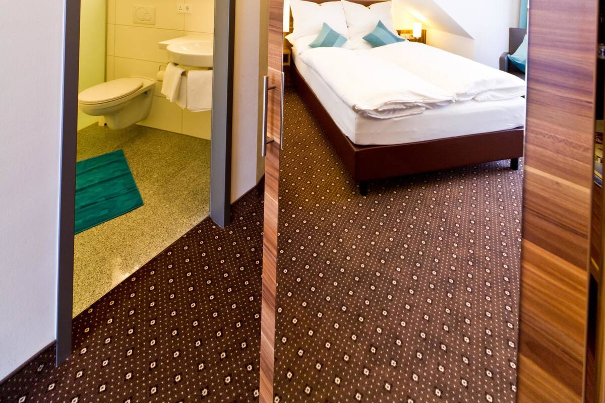 Een moderne hotelkamer met een groot bed, een badkamer met toilet en wastafel, en een spiegel die de kamer weerspiegelt.