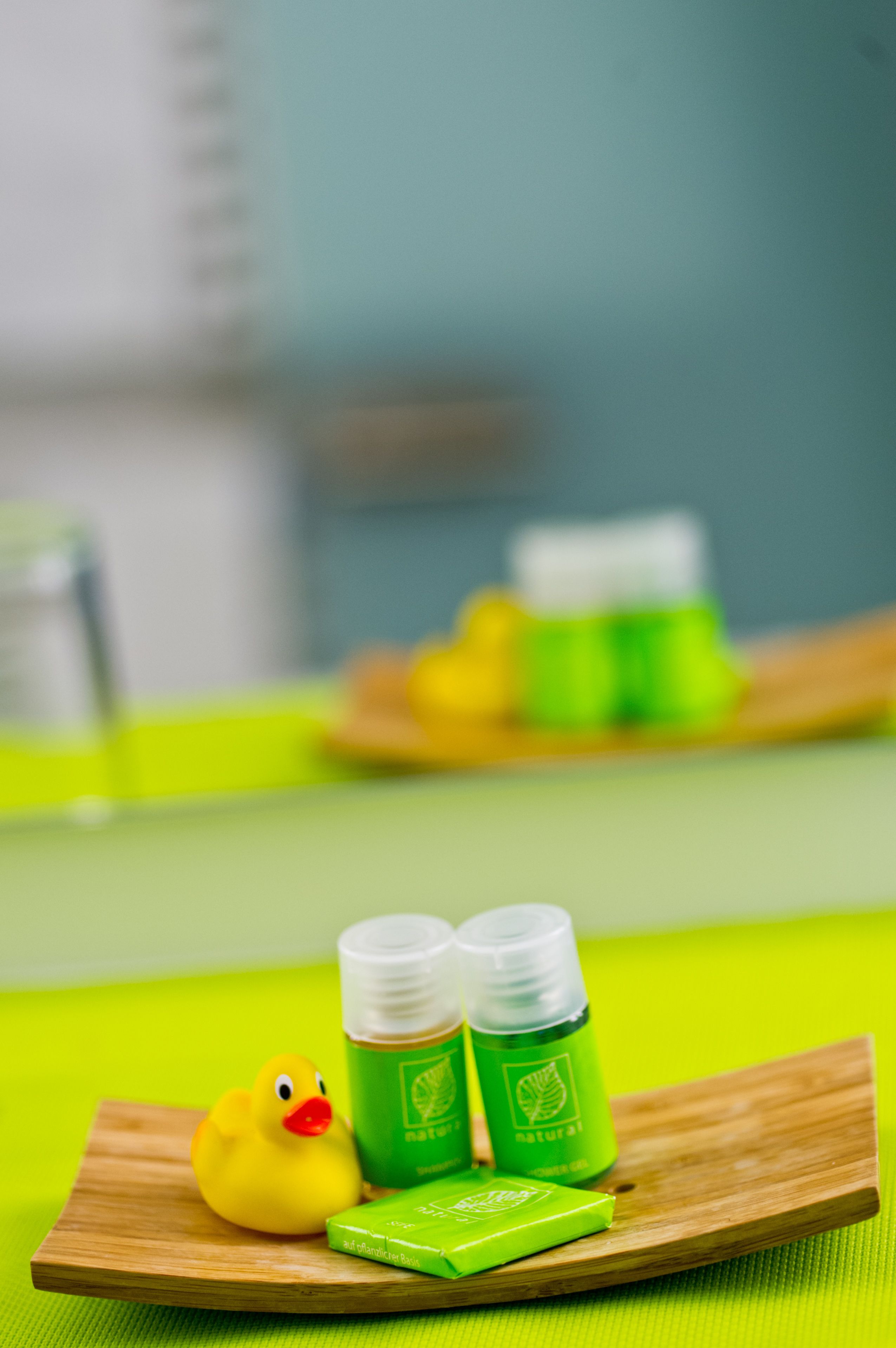 A wooden tray with a rubber duck, two green bottles, and a green packet on a bright green surface.