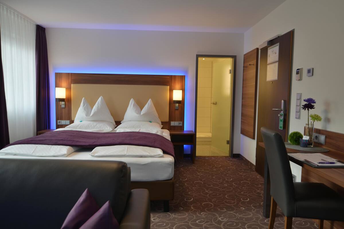 Een hotelkamer met een groot bed, een bureau en een stoel. Er is een deur die naar een andere kamer leidt.