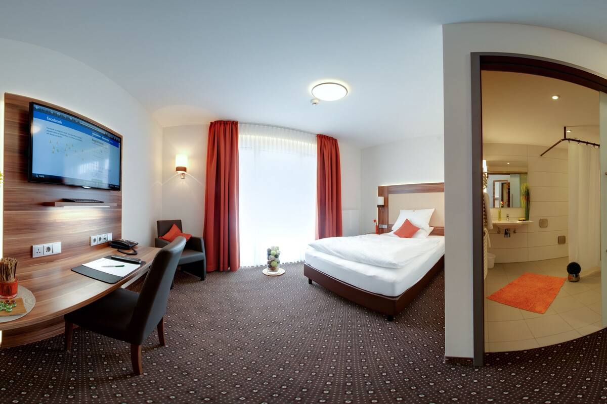 Een hotelkamer met een bed, bureau, stoel, televisie en een badkamer zichtbaar door een geopende deur.