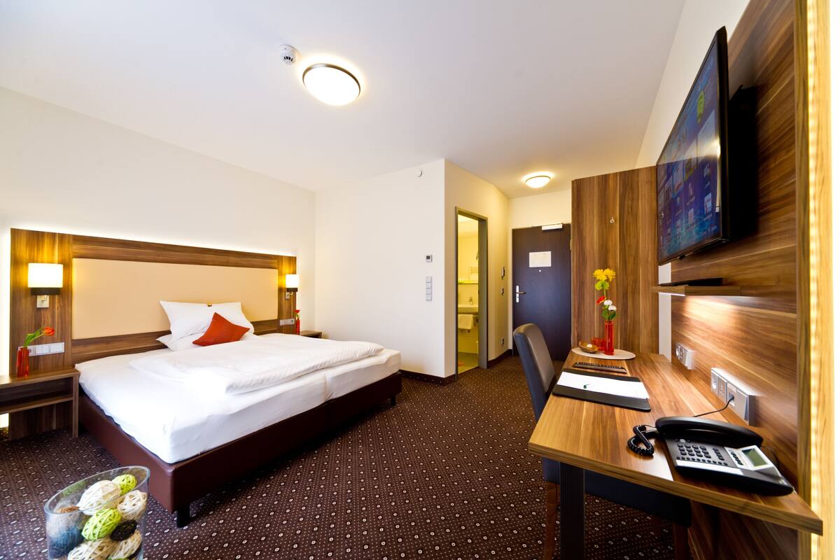 Een hotelkamer met een bed, nachtkastjes, een bureau met telefoon en een televisie aan de muur.