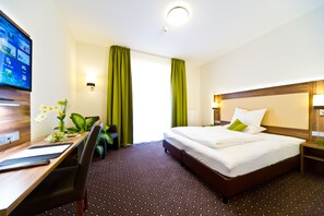 Habitación de hotel con cama, escritorio, silla y televisión en la pared.