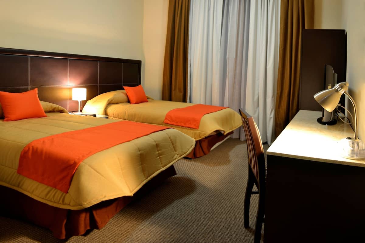 Ein Hotelzimmer mit zwei Betten, einem Schreibtisch, einer Lampe und einem Fernseher.