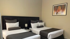 Habitación de hotel con dos camas, cada una con cabecero negro y ropa de cama blanca. Hay un cuadro en la pared y una mesita de noche con una lámpara entre las camas.