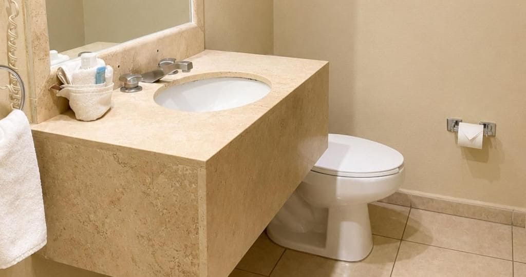A bathroom with a beige countertop, a sink, a toilet, and a towel rack.