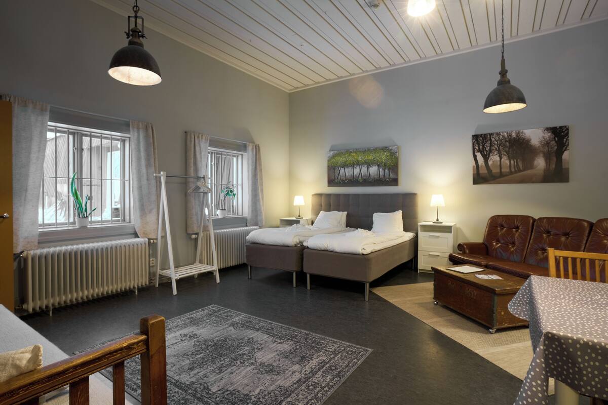 Moderni hotellihuone, jossa on parivuode, sohva, ruokapöytä ja suuri ikkuna, jossa on verhot.