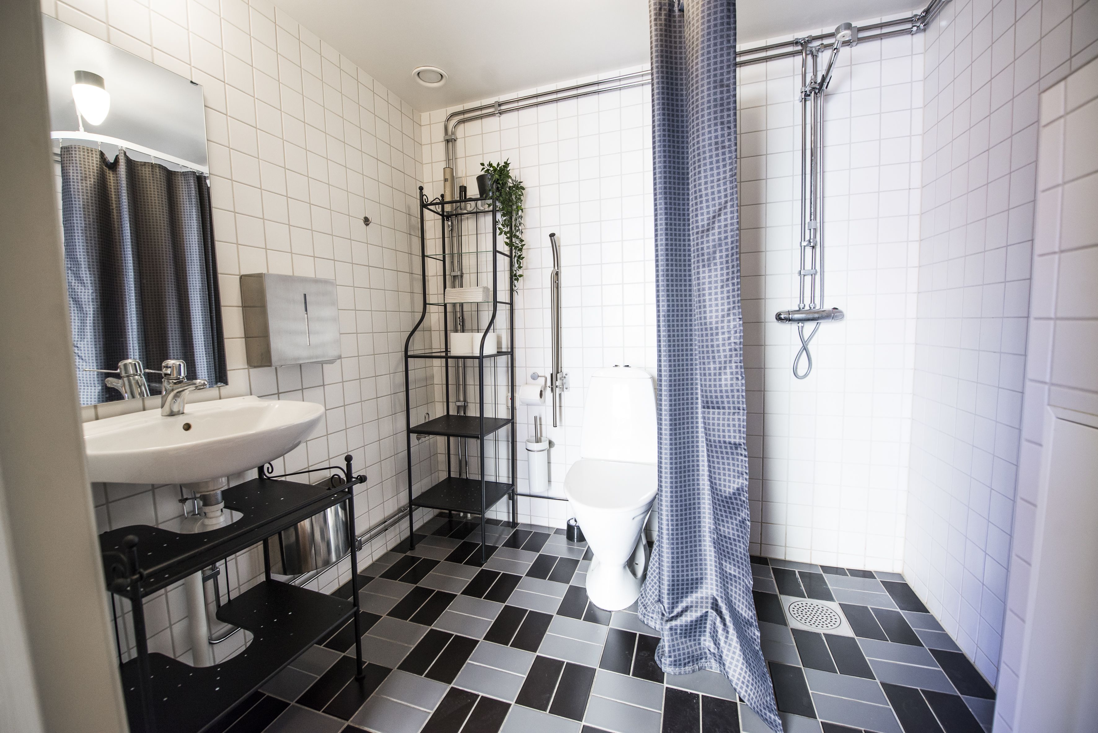 A bathroom with a white sink, black and white tiled floor, a shower with a blue shower curtain, and a white toilet.