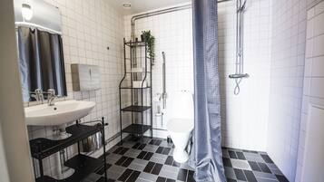 A bathroom with a white sink, black and white tiled floor, a shower with a blue shower curtain, and a white toilet.