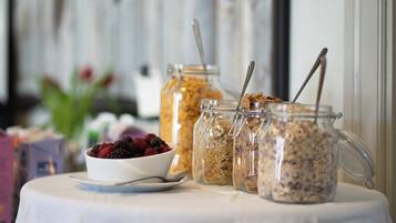 A breakfast table with a bowl of mixed berries, three glass jars of granola, and spoons.