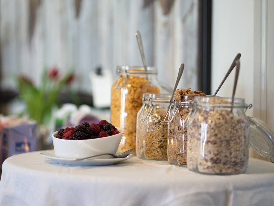 A breakfast table with a bowl of mixed berries, three glass jars of granola, and spoons.