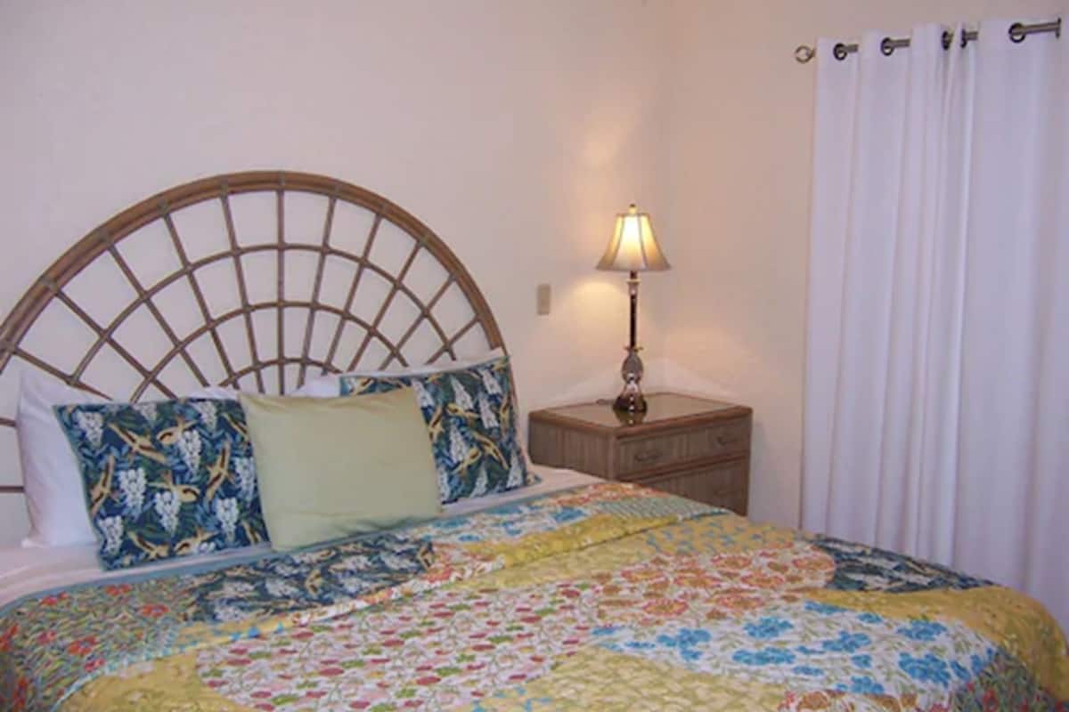 A bed with a wooden headboard, a bedside table with a lamp, and a floral bedspread.