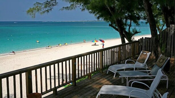 A beach with a wooden deck, white lounge chairs, and a view of the ocean. - Sunrise Beach Club and Villas (Paradise Island)