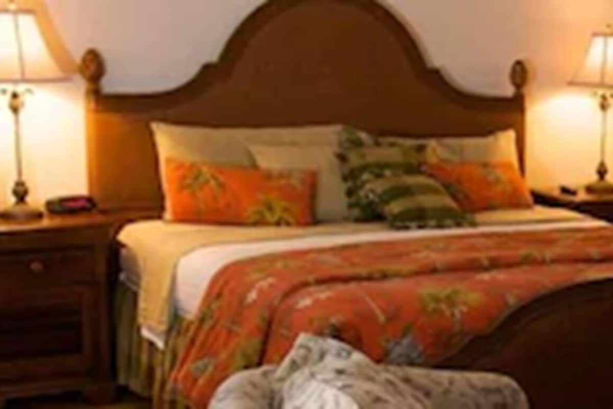 A neatly made bed with a wooden headboard, two bedside tables with lamps, and a chair with a cushion.