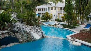 A pool area with a stone bridge, surrounded by lush greenery and a building with balconies. - Sunrise Beach Club and Villas (Paradise Island)
