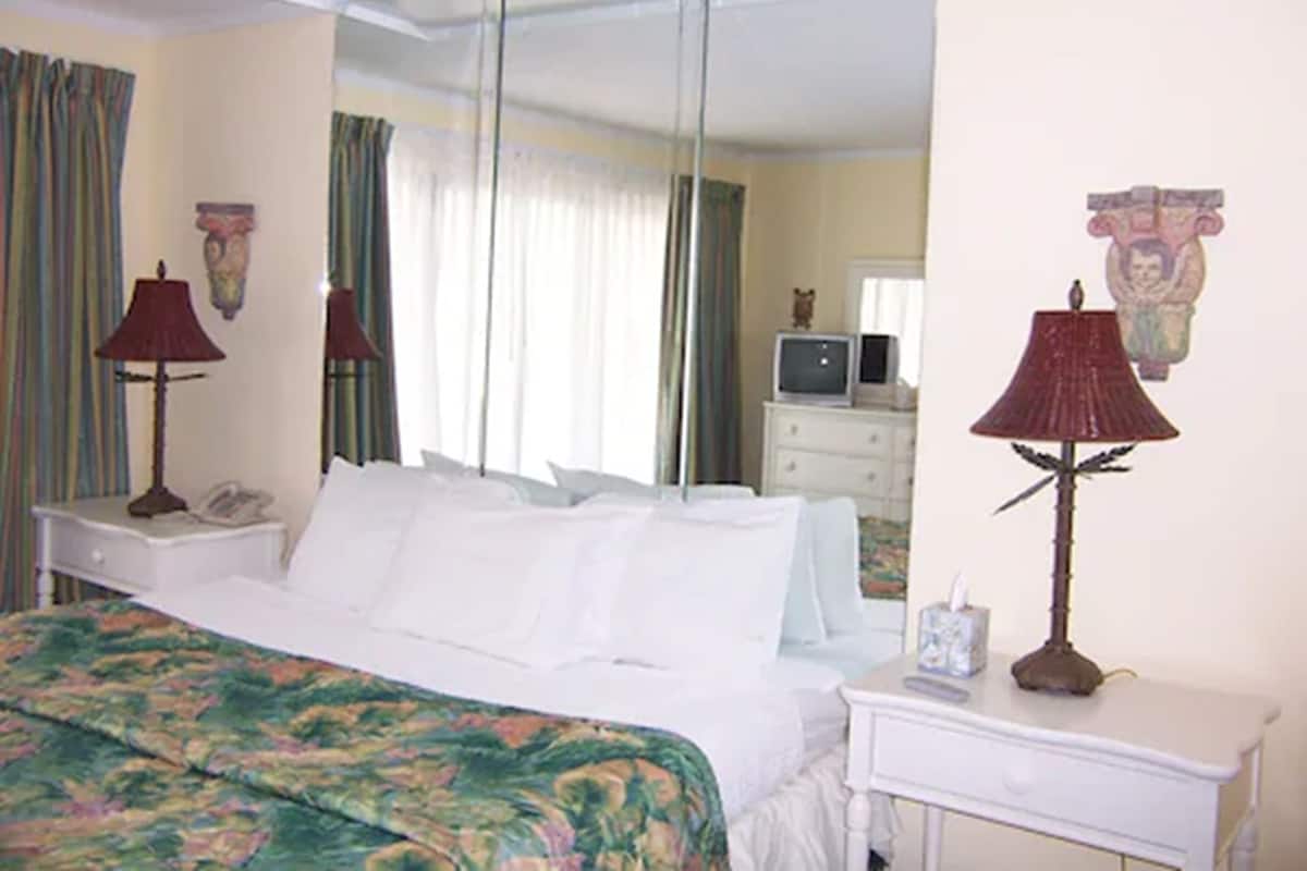 A hotel room with a bed, a nightstand, a lamp, a dresser, a television, and a mirror.