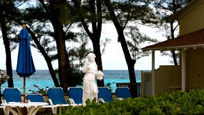 A statue of a woman holding a bouquet, a blue umbrella, and a poolside setting with chairs and a view of the ocean. - Sunrise Beach Club and Villas (Paradise Island)
