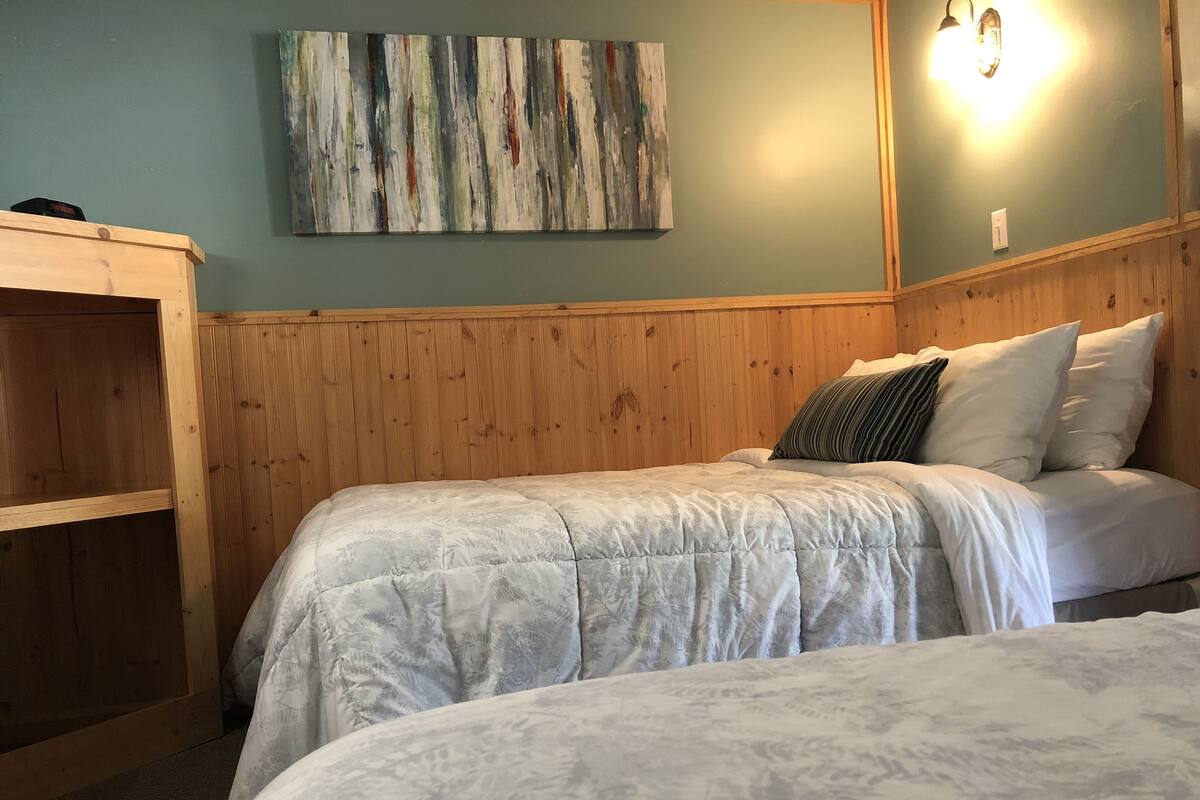 A room with a bed, a wooden headboard, a wall-mounted light fixture, and a piece of abstract art.