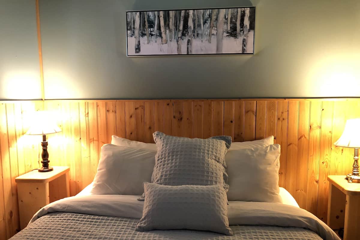 A bedroom with a wooden headboard, a bed with white bedding, two bedside lamps, and a framed picture on the wall.