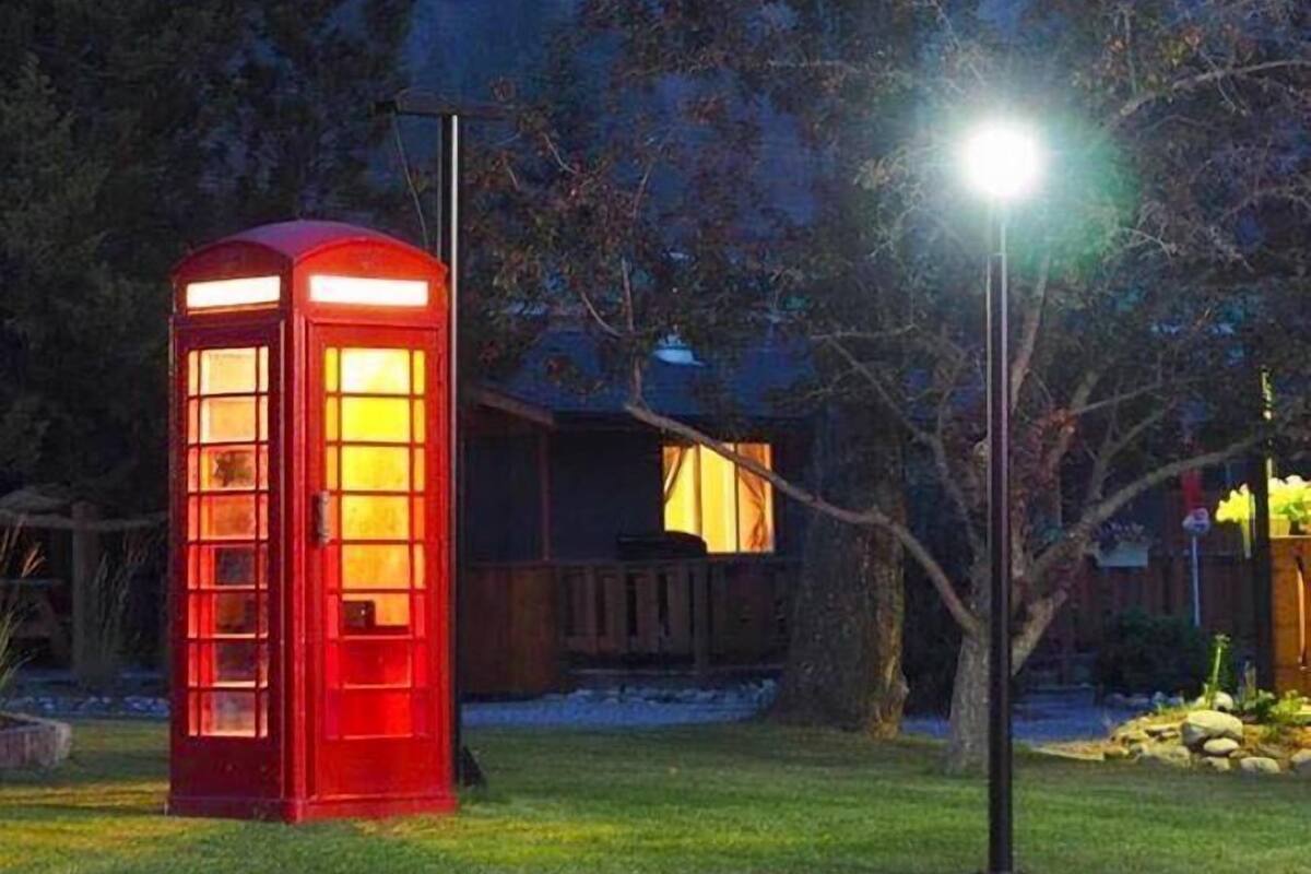 A red telephone booth in a garden setting with a house in the background.