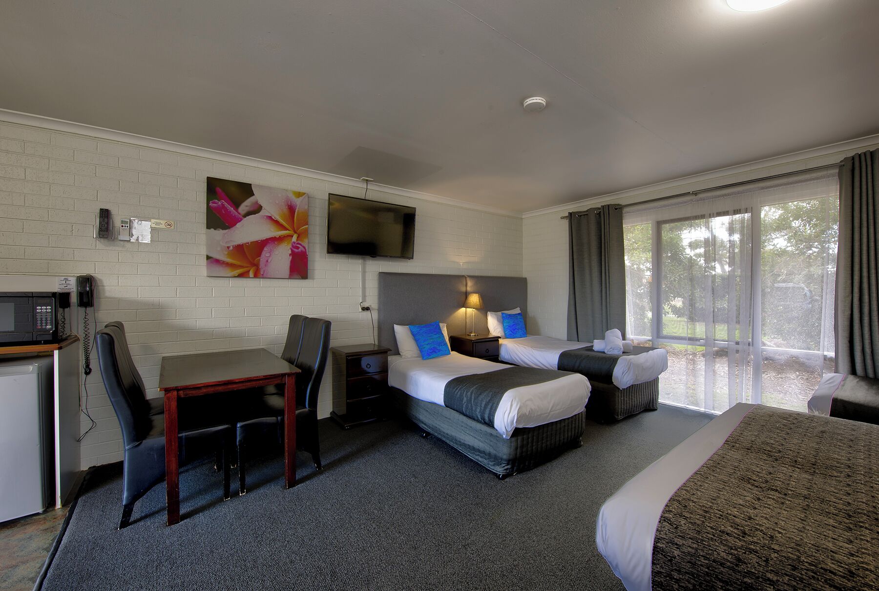 Habitación de hotel con dos camas, un escritorio, una silla, un televisor y una ventana con cortinas.