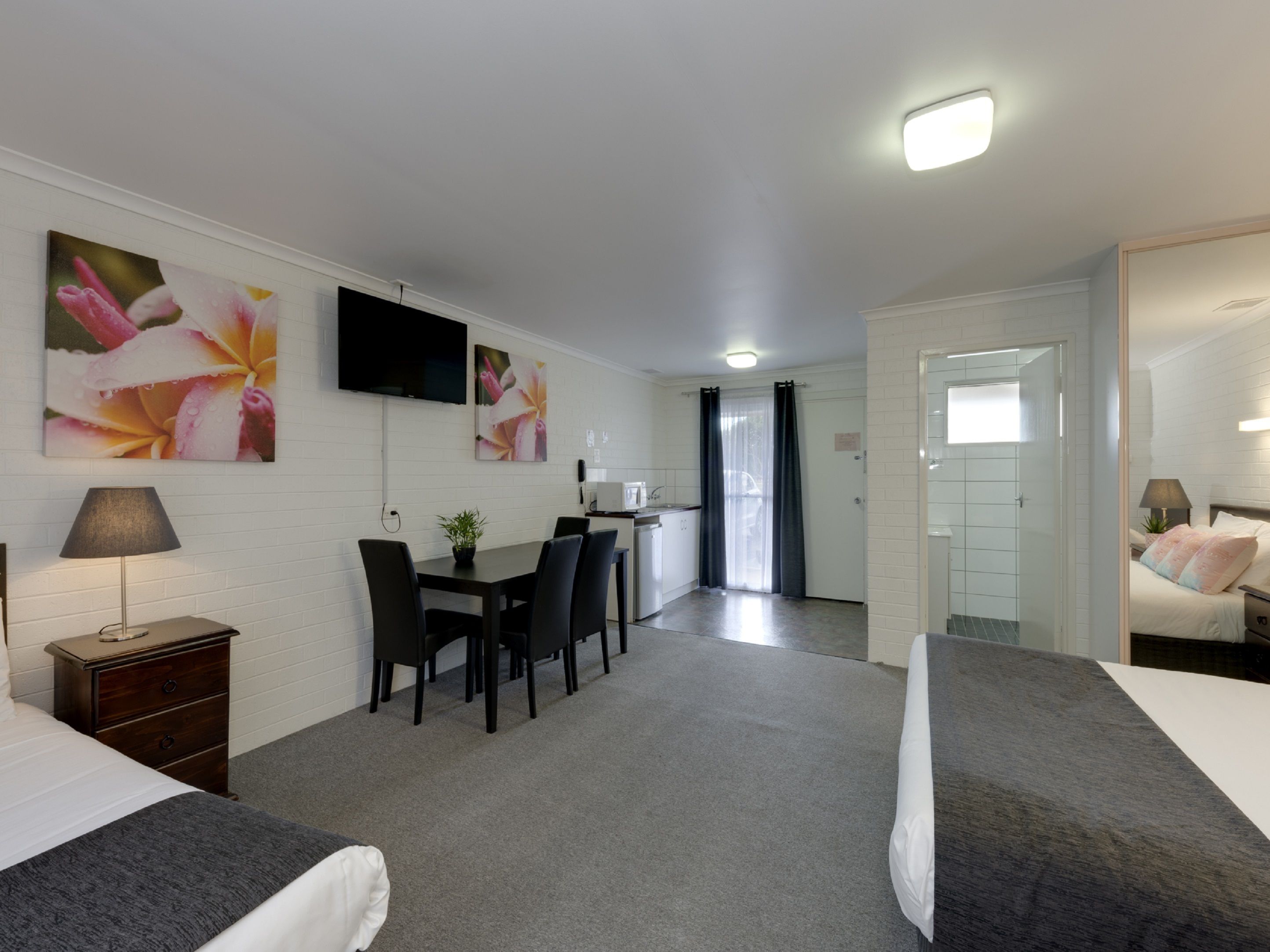 Ein Hotelzimmer mit einem Bett, einem Schreibtisch mit Stühlen, einem an der Wand befestigten Fernseher und einem durch eine offene Tür einsehbaren Badezimmer.