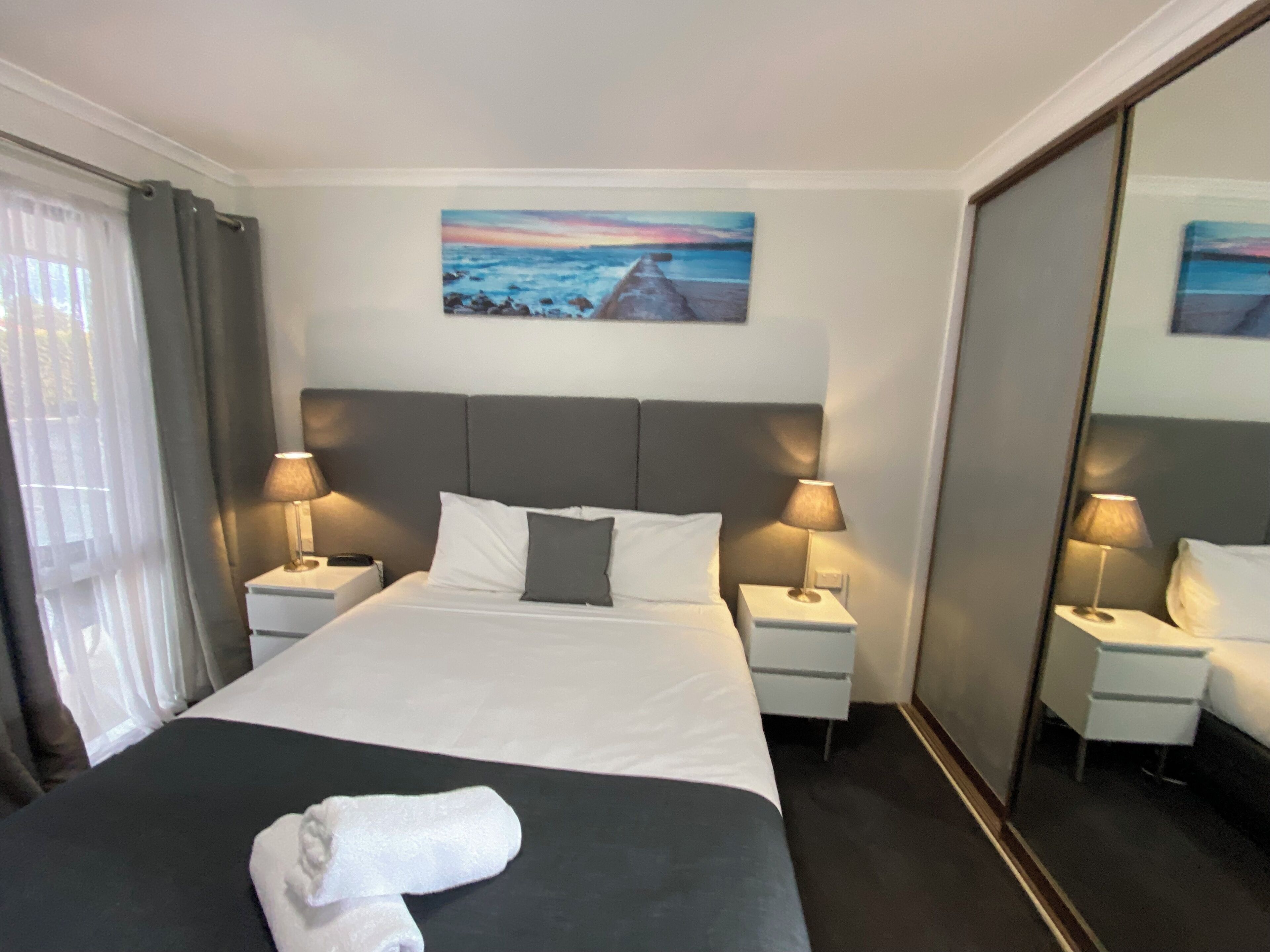 Une chambre d’hôtel avec un grand lit, deux tables de chevet avec des lampes, un tableau au mur et un miroir.
