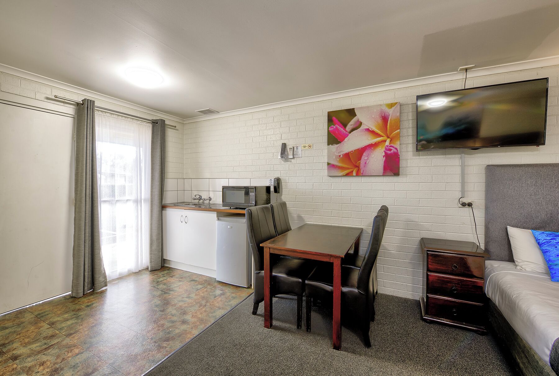 A compact room with a kitchenette, a dining area, a bed, and a TV.