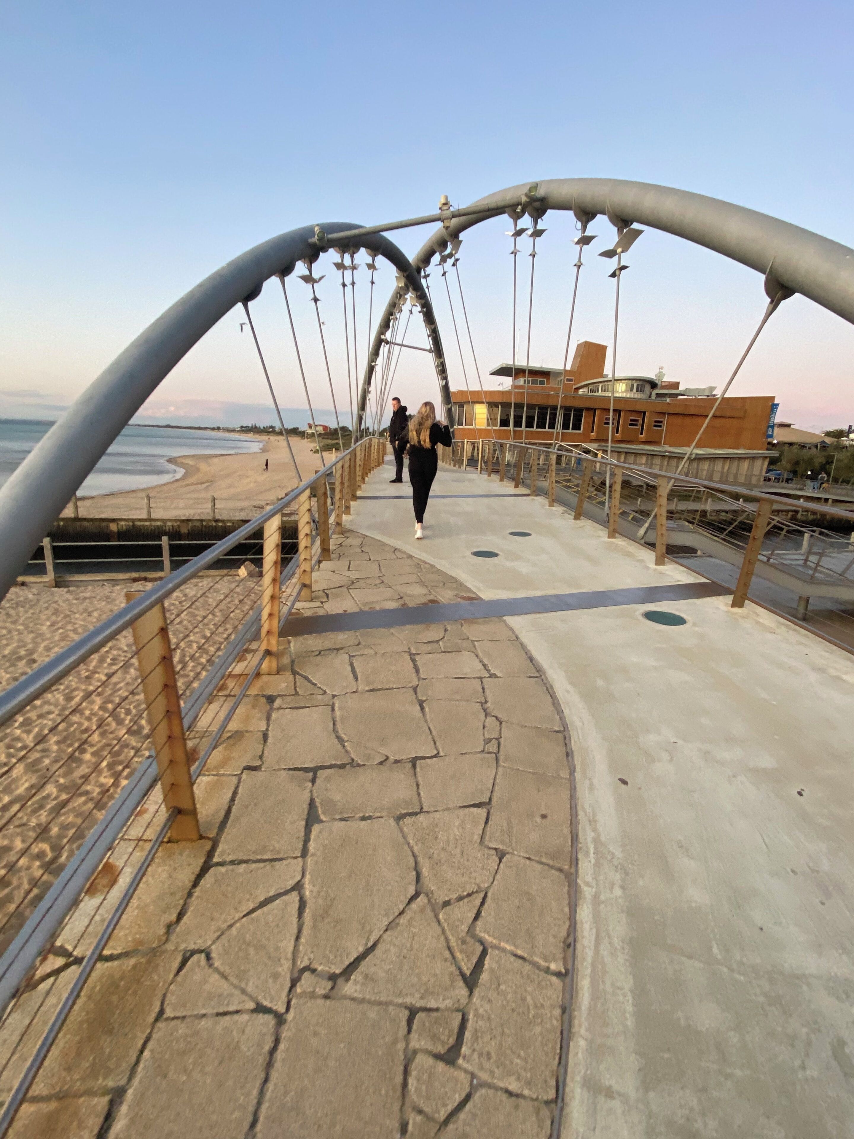Un ponte pedonale con arco in metallo e percorso in pietra che conduce a una spiaggia.