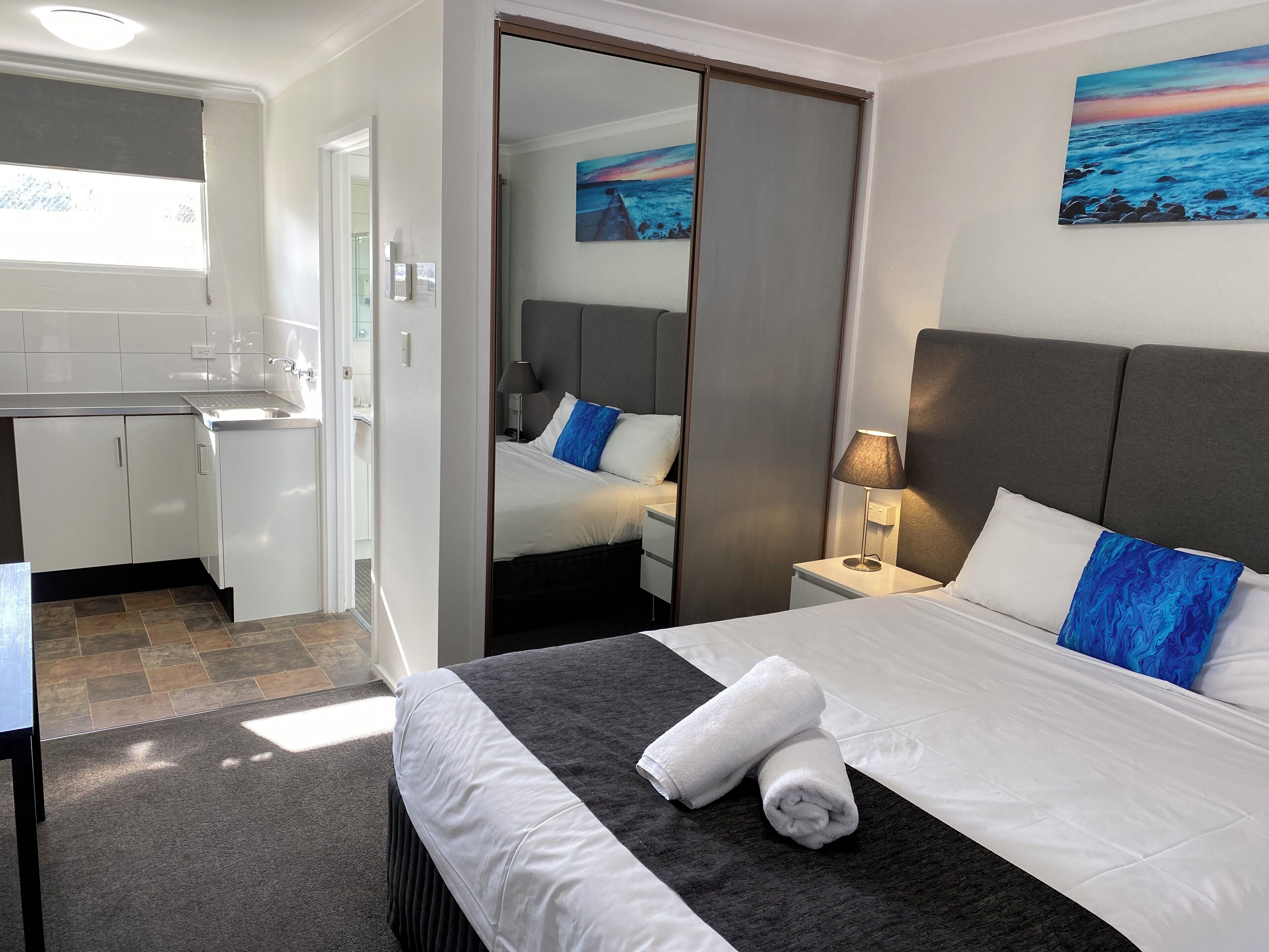 Una habitación de hotel con cama, escritorio, espejo y un cuadro en la pared.