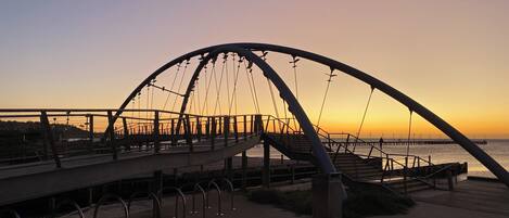 A pedestrian bridge with a curved metal arch design, connecting two land masses over a body of water.