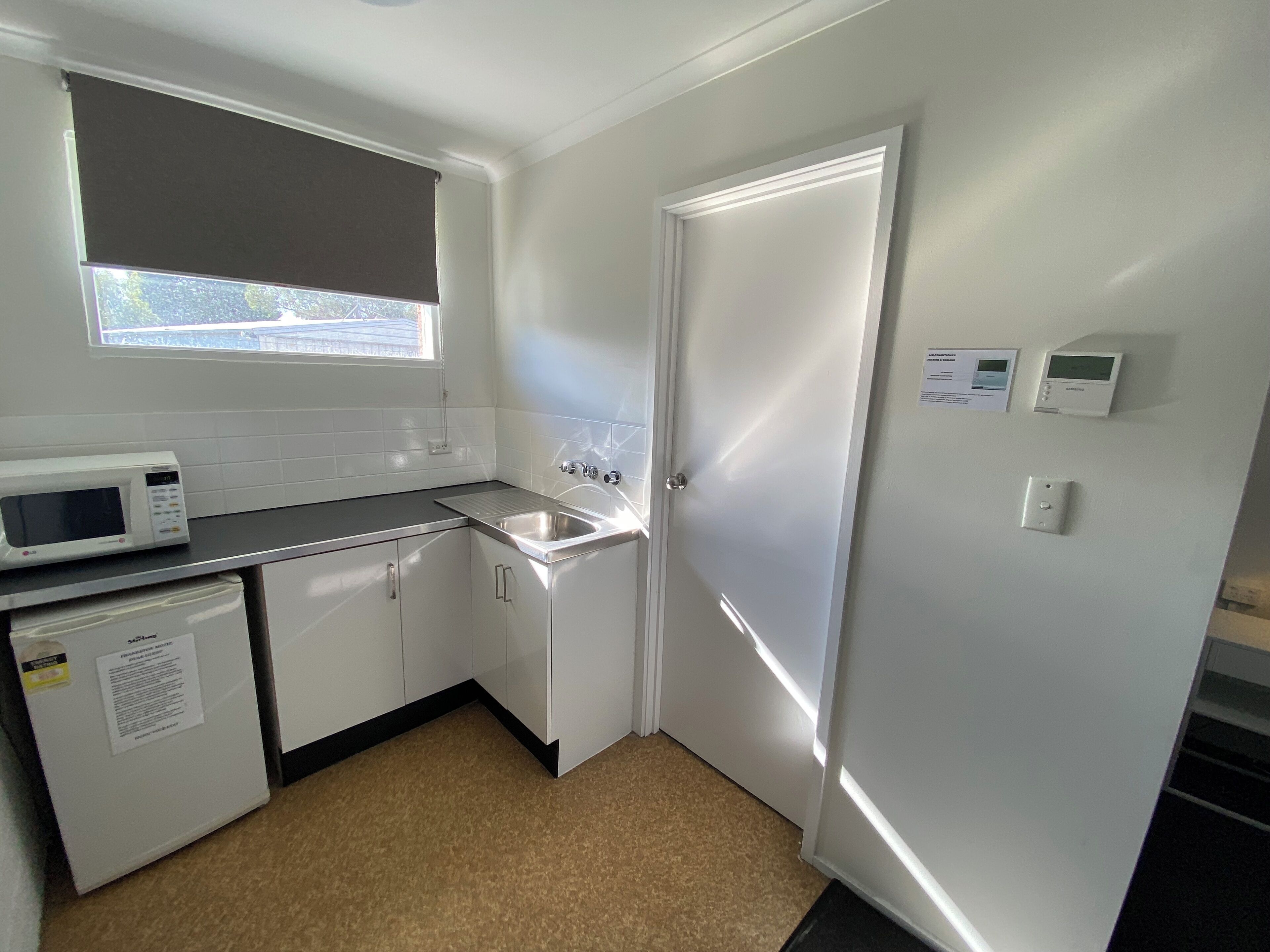 Una cocina compacta con armarios blancos, microondas, lavamanos y refrigerador.