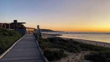 Un muelle de madera que conduce a una playa con un espigón que se adentra en el agua.