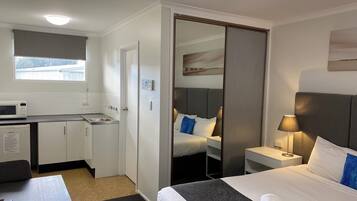 A hotel room with a bed, bedside table, lamp, and a kitchenette with a microwave.