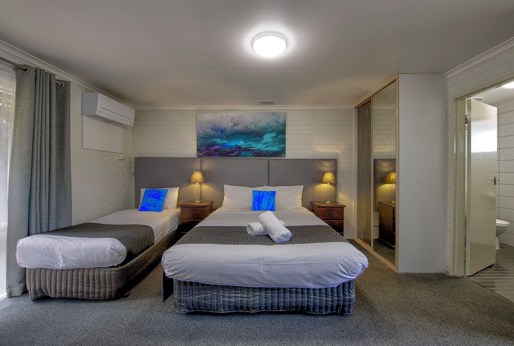 Une chambre d’hôtel avec deux lits, un grand tableau et un luminaire au plafond.