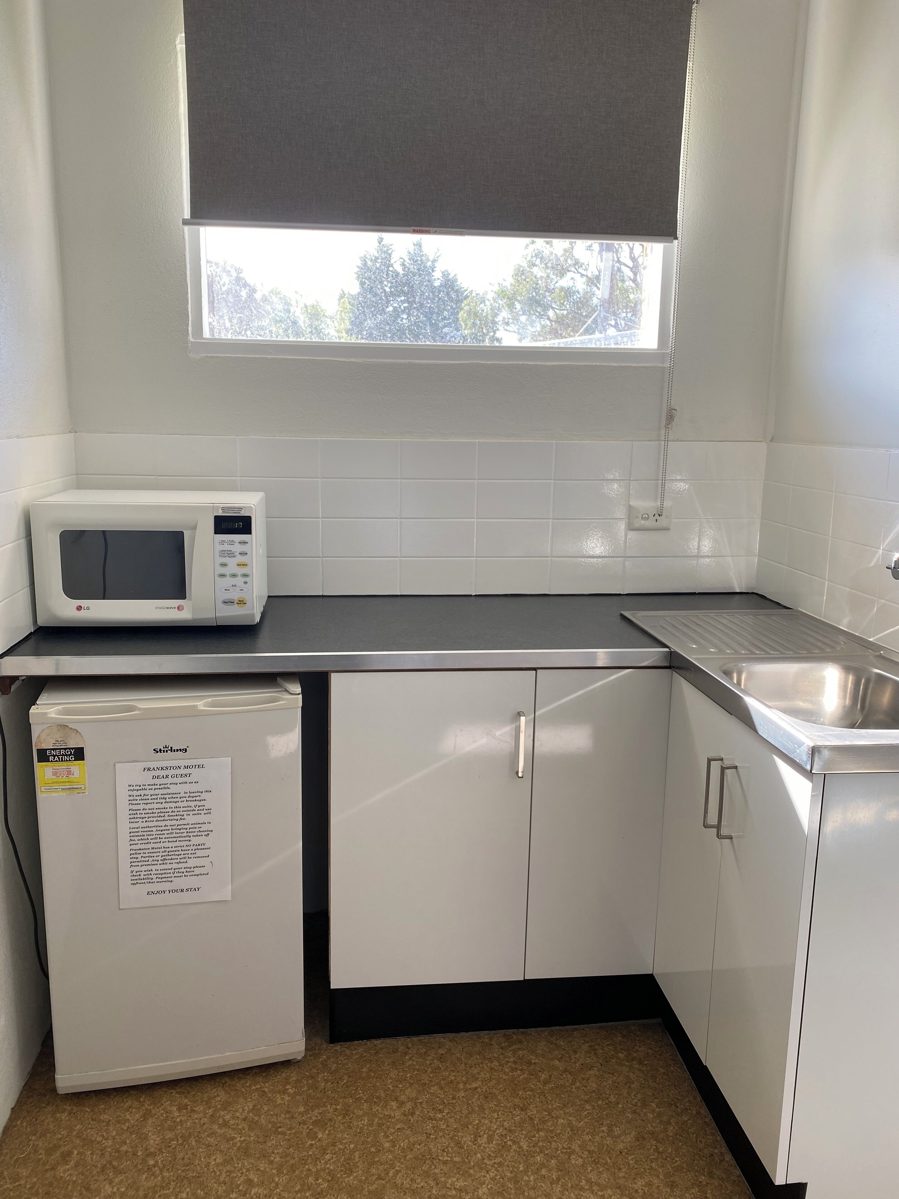 Una kitchenette compacta con microondas, un refrigerador pequeño, un lavamanos y una ventana sobre la encimera.
