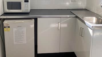 Una kitchenette compacta con microondas, un refrigerador pequeño, un lavamanos y una ventana sobre la encimera.