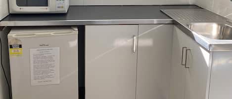 A compact kitchenette with a microwave, a small refrigerator, a sink, and a window above the counter.