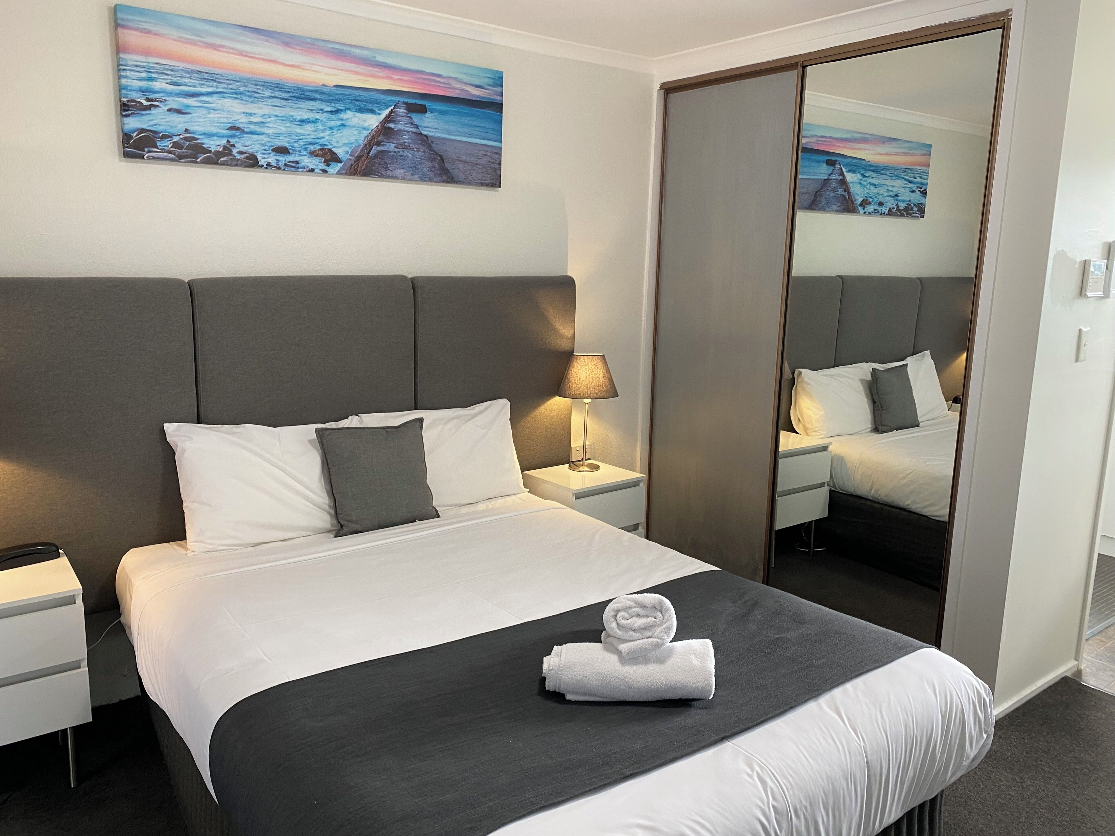 Une chambre d’hôtel avec un grand lit, une table de chevet, une lampe, un miroir et des œuvres d’art accrochées au mur.