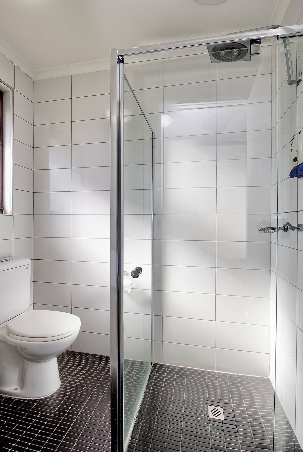 Une salle de bain moderne avec une douche à parois de verre, des murs recouverts de carreaux blancs et des toilettes.