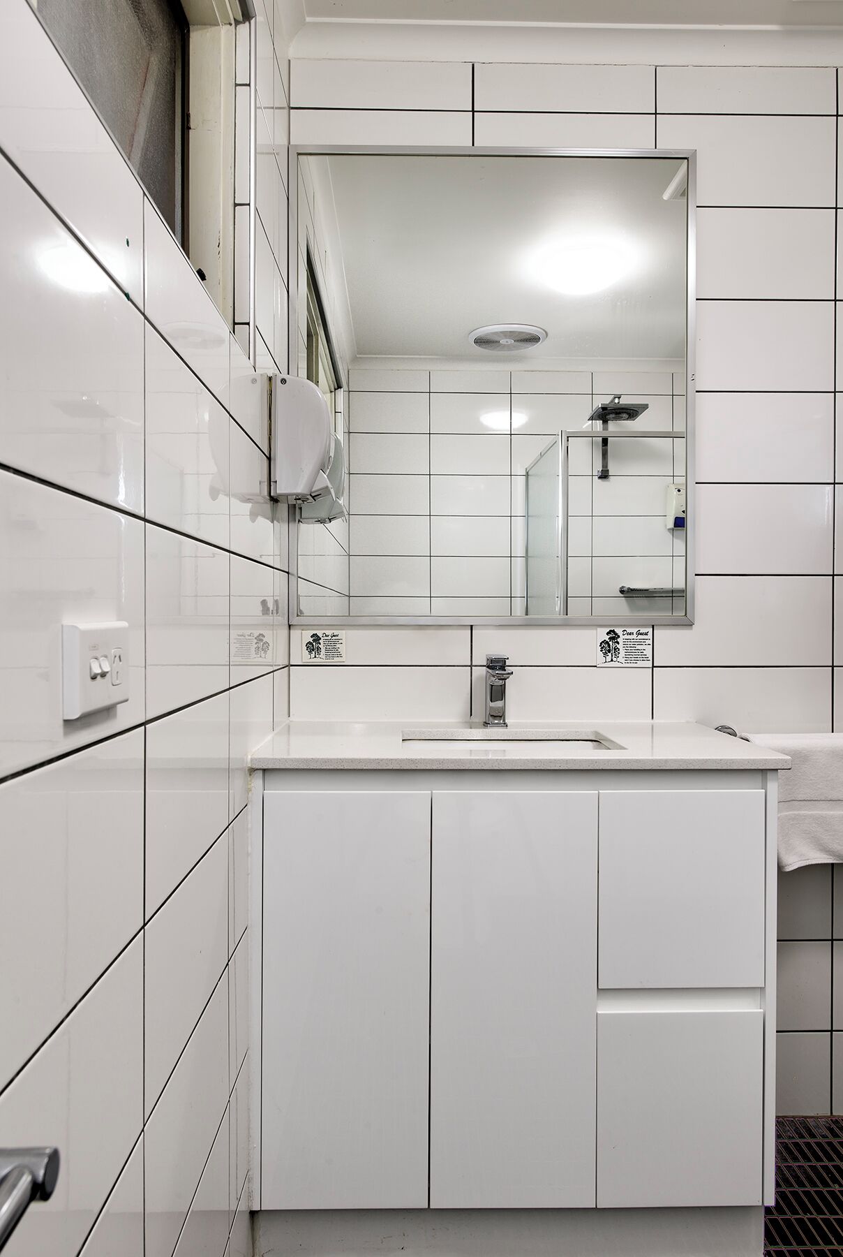 Un baño moderno con azulejos blancos, un espejo grande, un lavabo y un perchero para toallas.