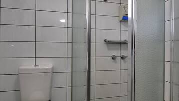 Un baño con inodoro, ducha con puerta de cristal y paredes de azulejos.