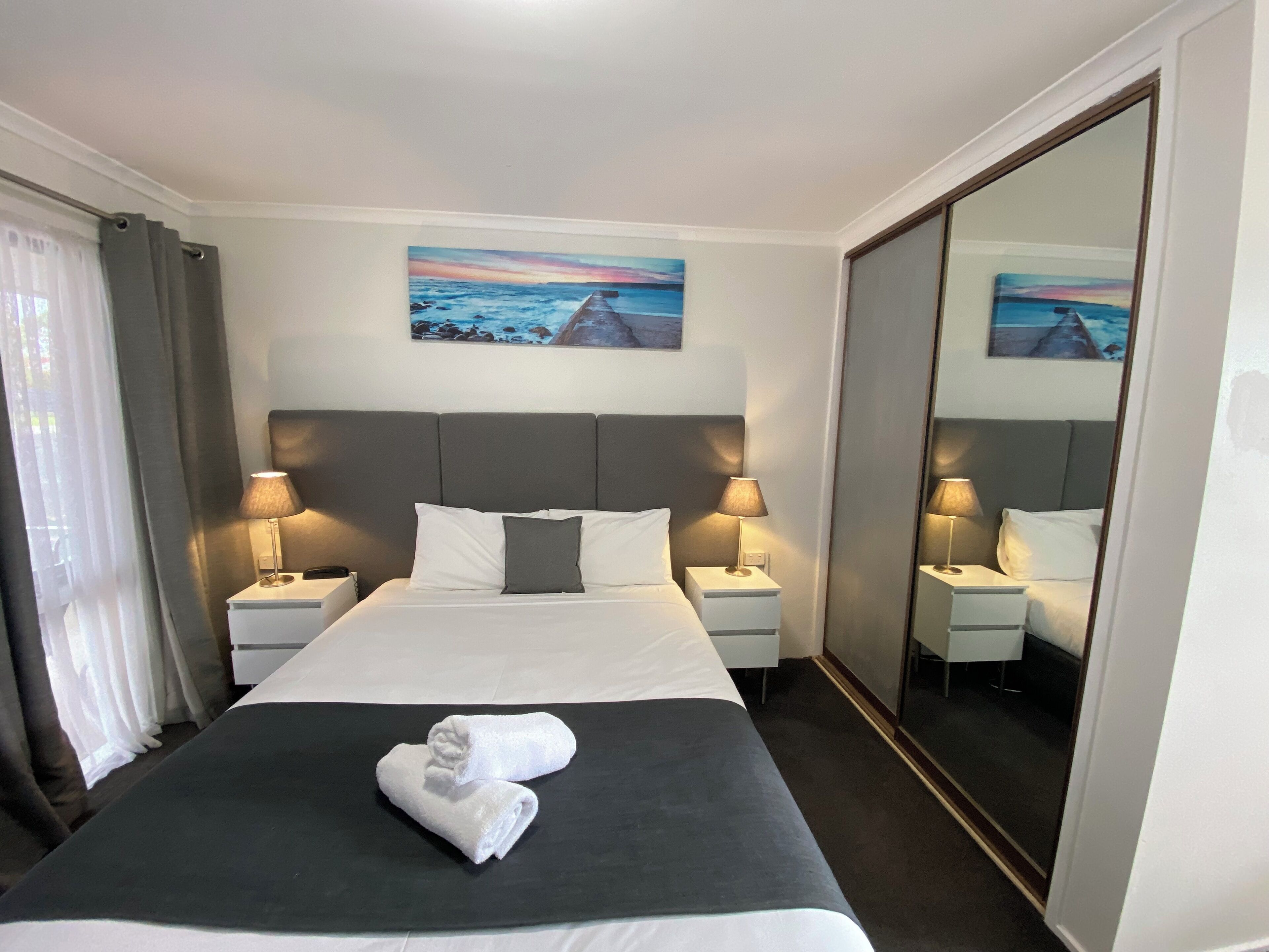 Una camera d'albergo con un letto grande, due comodini con lampade, un quadro appeso al muro e un ampio specchio.