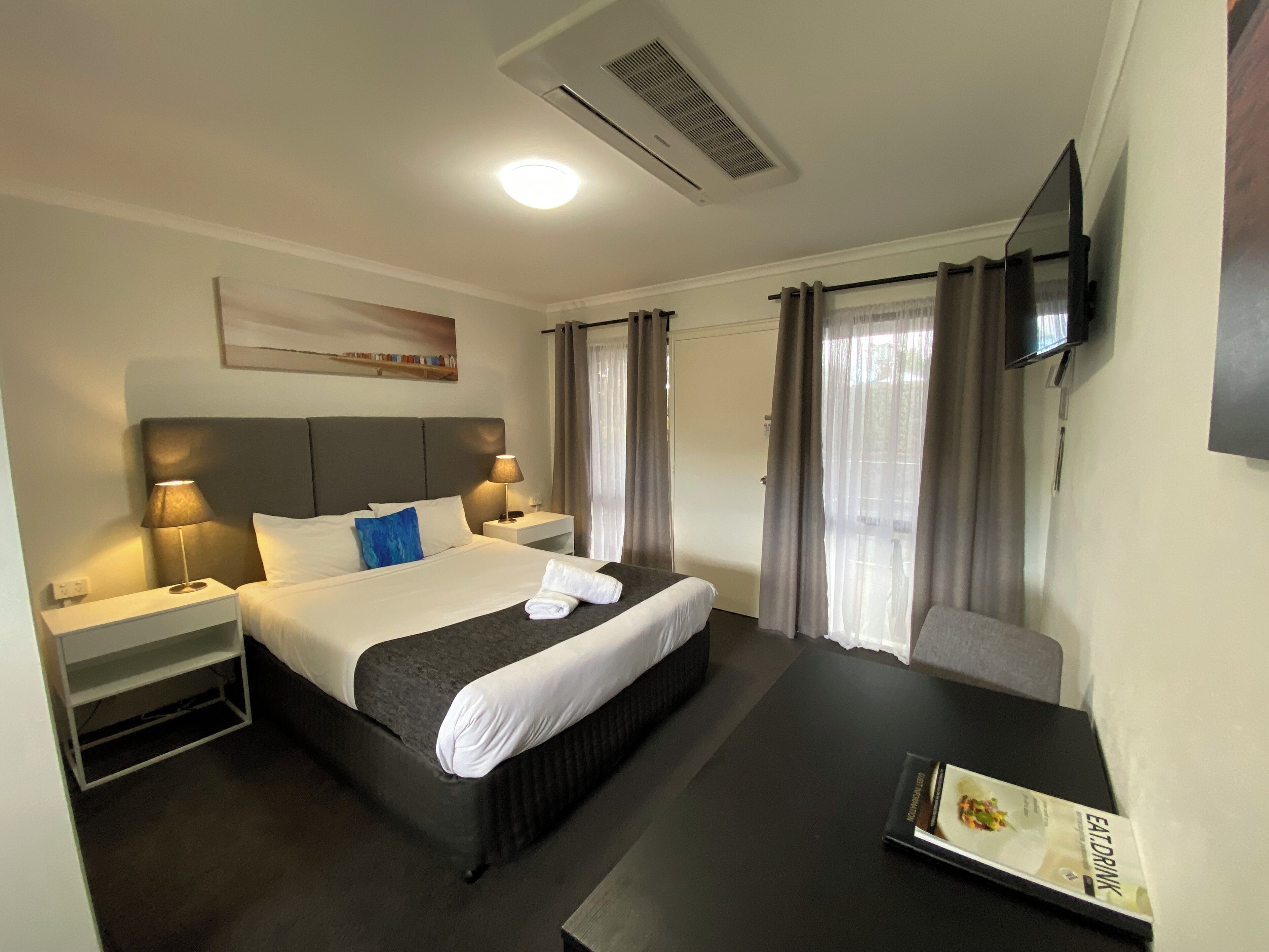 Una habitación de hotel con cama, mesitas de noche, escritorio, televisión y cortinas.