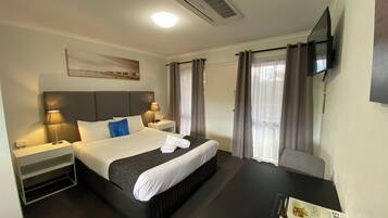 Una habitación de hotel con cama, mesitas de noche, escritorio, televisión y cortinas.