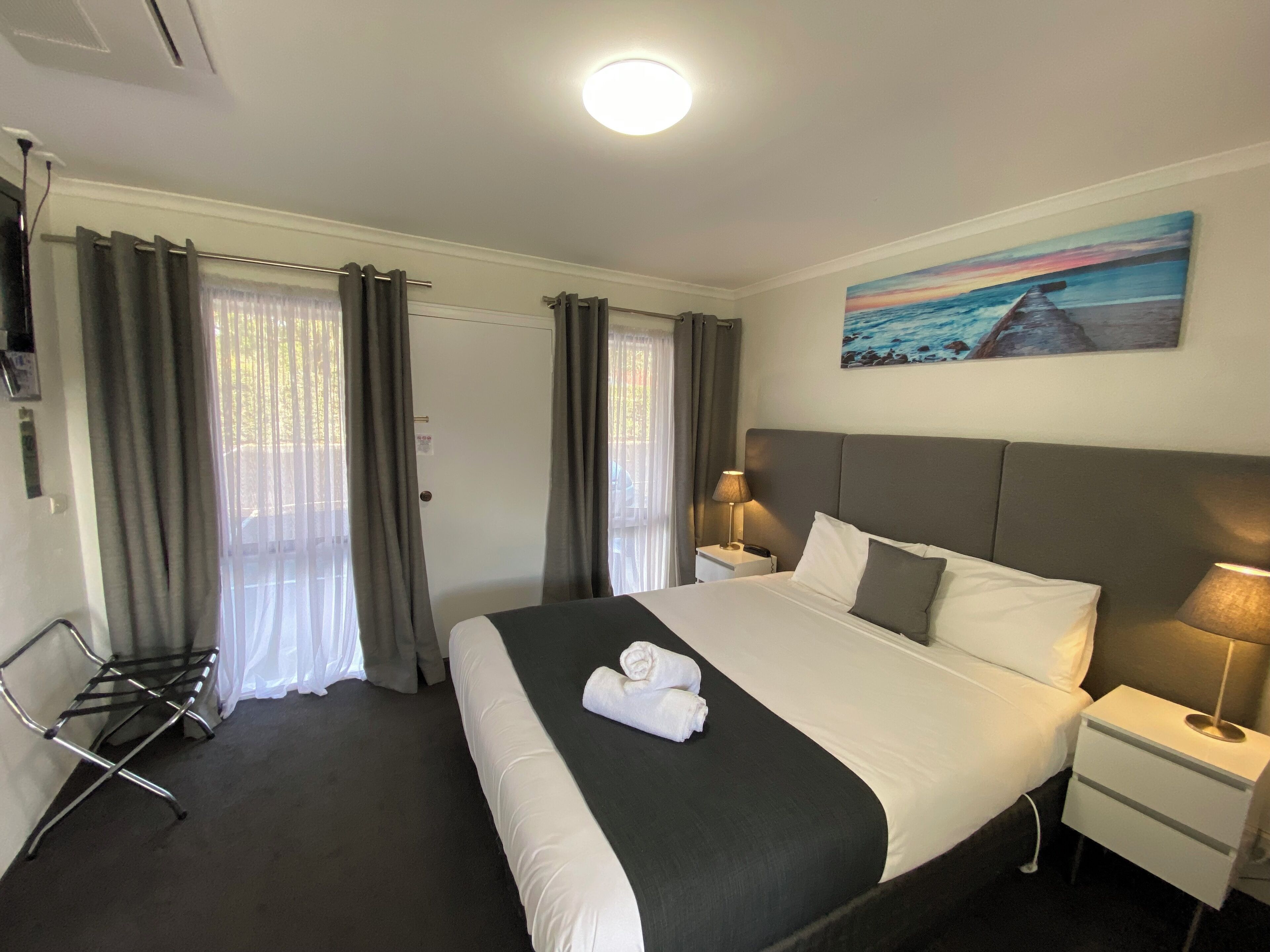 Een hotelkamer met een groot bed, twee nachtkastjes met lampen, een schilderij aan de muur en een raam met gordijnen.